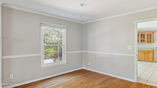 unfurnished room featuring a wealth of natural light, a wainscoted wall, visible vents, and light wood-style flooring