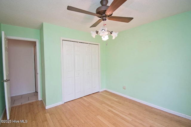 unfurnished bedroom featuring baseboards, light wood-style floors, a closet, a textured ceiling, and a ceiling fan