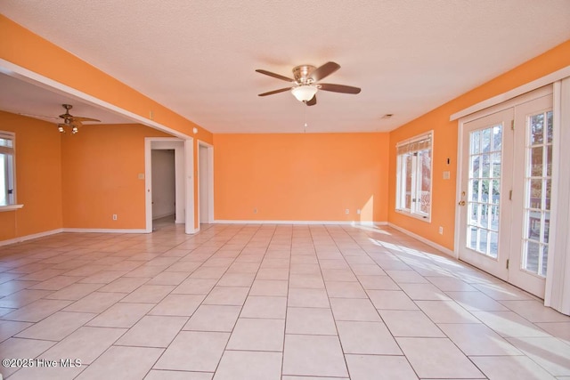 empty room with light tile patterned flooring, a ceiling fan, baseboards, and a textured ceiling