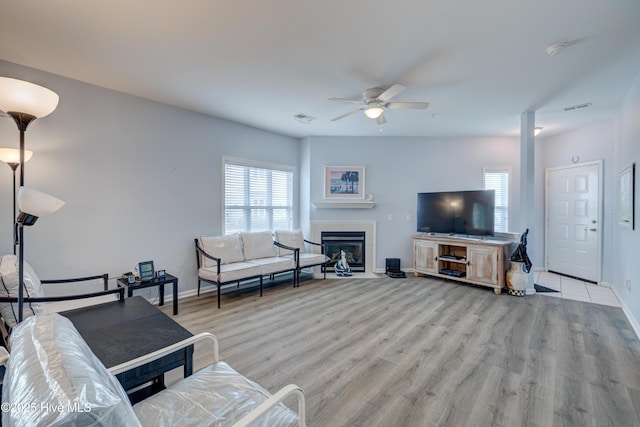 living room with light wood-style floors, a fireplace with flush hearth, visible vents, and a healthy amount of sunlight