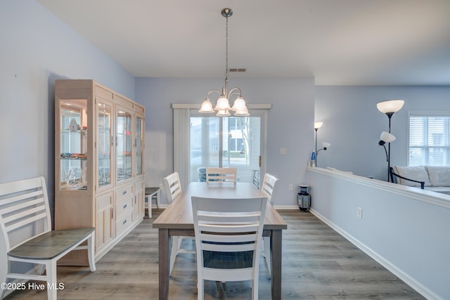 dining area with baseboards, wood finished floors, visible vents, and an inviting chandelier