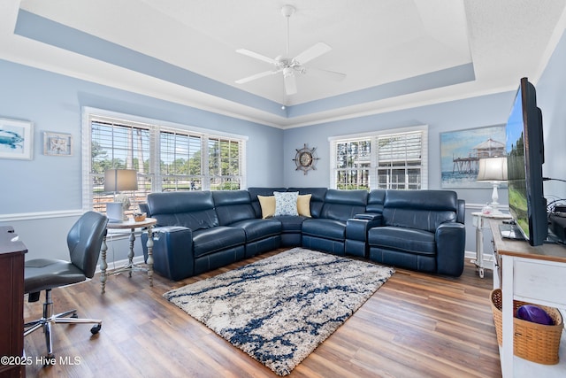 living area featuring ceiling fan, a raised ceiling, a wealth of natural light, and wood finished floors