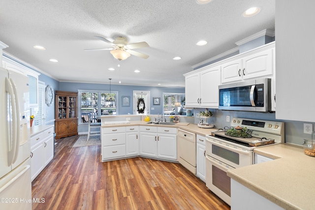 kitchen with light wood finished floors, white cabinetry, a sink, white appliances, and a peninsula