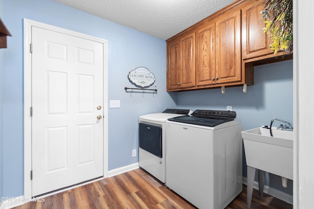 washroom featuring cabinet space, baseboards, wood finished floors, a textured ceiling, and washing machine and dryer