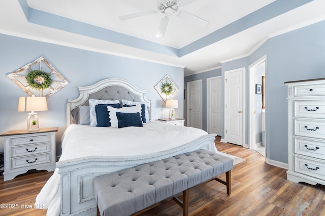 bedroom with baseboards, a tray ceiling, wood finished floors, and ornamental molding