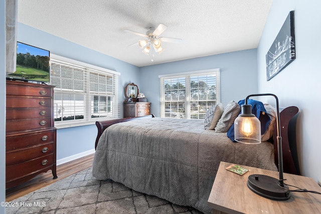 bedroom featuring a ceiling fan, a textured ceiling, baseboards, and wood finished floors