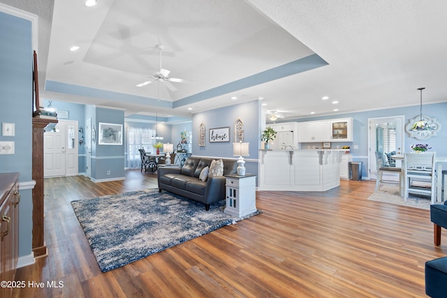 living room with light wood-style flooring, a tray ceiling, and a ceiling fan