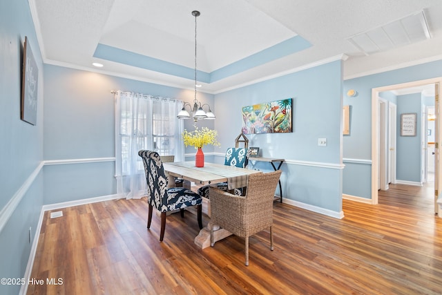 dining area featuring a tray ceiling, a notable chandelier, visible vents, wood finished floors, and baseboards