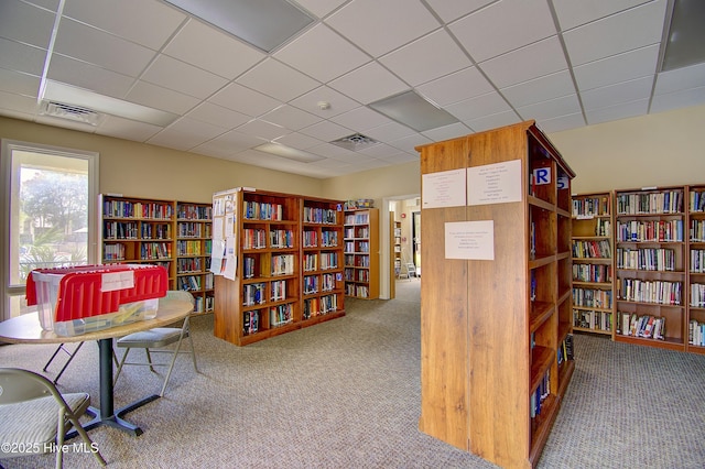 carpeted home office featuring wall of books, visible vents, and a paneled ceiling