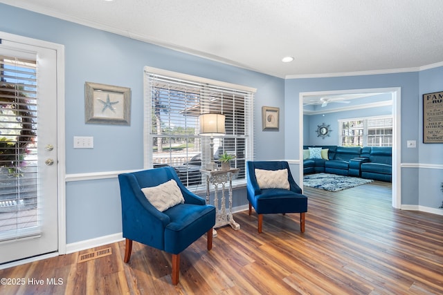 living area with visible vents, crown molding, a textured ceiling, and wood finished floors