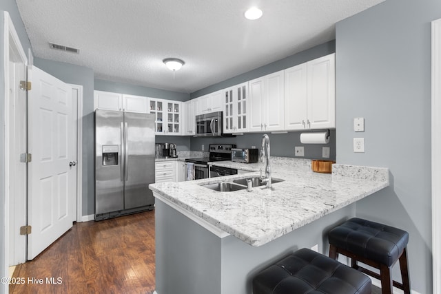 kitchen with visible vents, glass insert cabinets, a peninsula, stainless steel appliances, and a sink