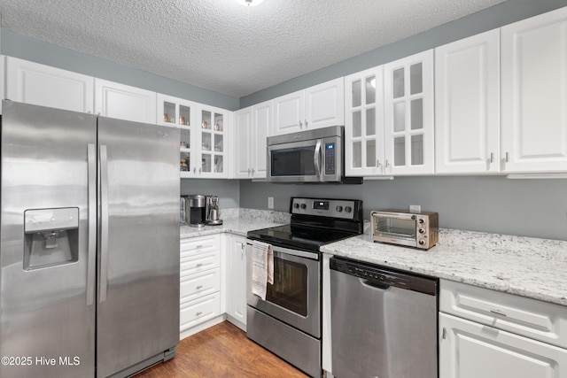 kitchen with a toaster, glass insert cabinets, wood finished floors, stainless steel appliances, and white cabinetry