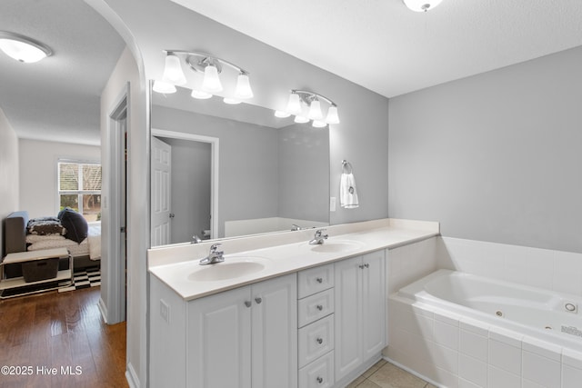 ensuite bathroom featuring double vanity, ensuite bath, a tub with jets, and a sink