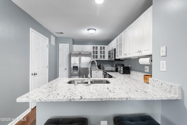 kitchen with glass insert cabinets, light stone counters, a peninsula, stainless steel appliances, and white cabinetry