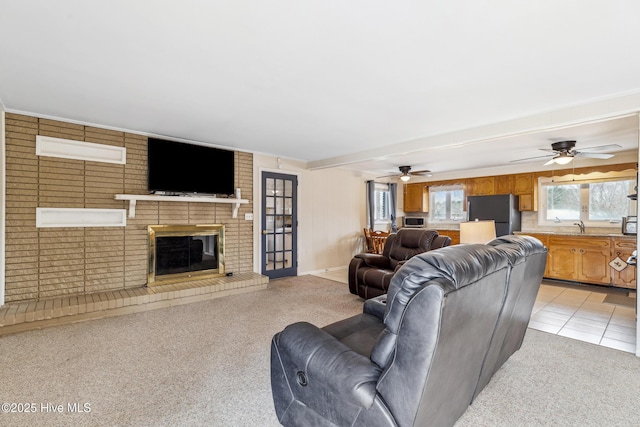 living area featuring ceiling fan, light carpet, a brick fireplace, and light tile patterned flooring