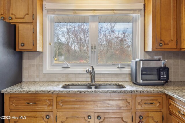 kitchen featuring decorative backsplash, brown cabinetry, freestanding refrigerator, and a sink