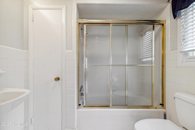 full bath featuring combined bath / shower with glass door, toilet, and tile walls