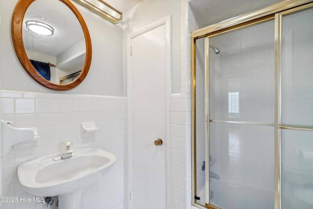 full bathroom with a tile shower, wainscoting, tile walls, and a sink