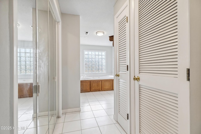 hallway featuring light tile patterned floors, visible vents, and baseboards