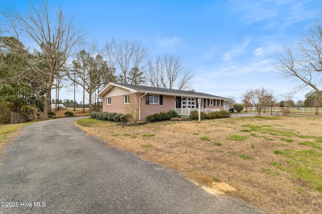 view of front of property with brick siding, covered porch, aphalt driveway, and fence