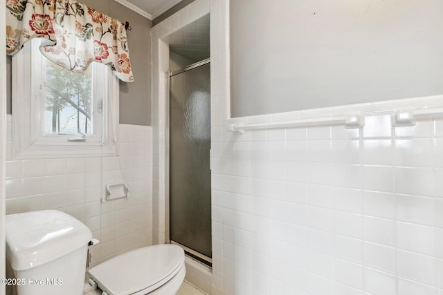 full bathroom featuring a wainscoted wall, toilet, a stall shower, ornamental molding, and tile walls