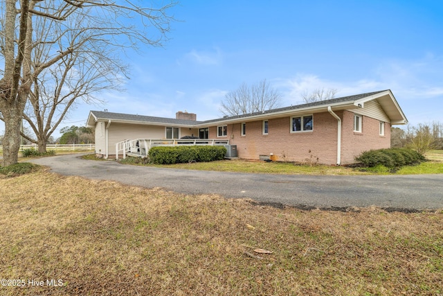 single story home featuring brick siding, cooling unit, a chimney, and a front lawn