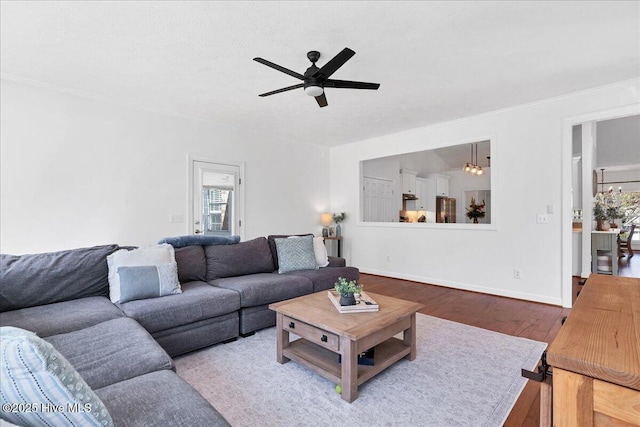 living area featuring hardwood / wood-style floors, ceiling fan with notable chandelier, and baseboards