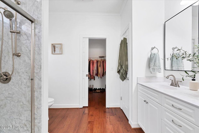 bathroom featuring a shower stall, baseboards, ornamental molding, wood finished floors, and vanity