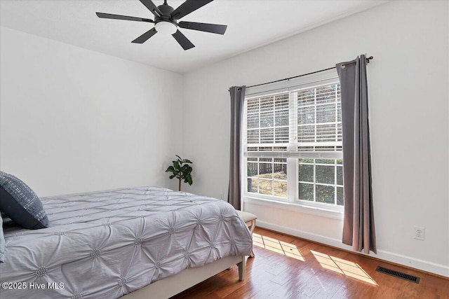 bedroom with a ceiling fan, wood finished floors, visible vents, and baseboards