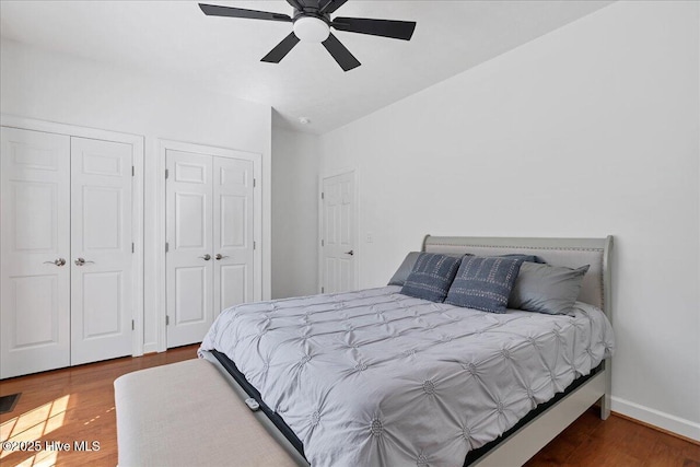 bedroom featuring wood finished floors, baseboards, two closets, and ceiling fan