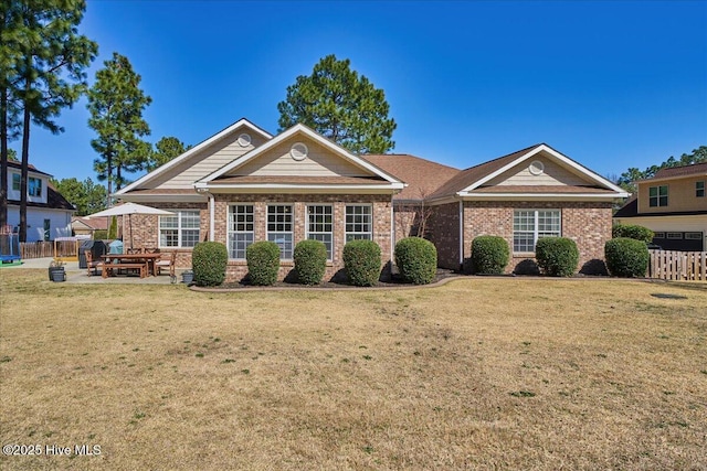 view of front of home with a patio area, brick siding, a front lawn, and fence