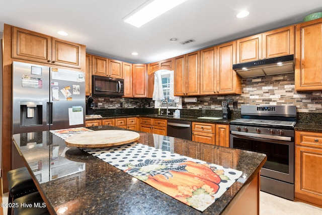 kitchen featuring visible vents, decorative backsplash, appliances with stainless steel finishes, under cabinet range hood, and a kitchen bar