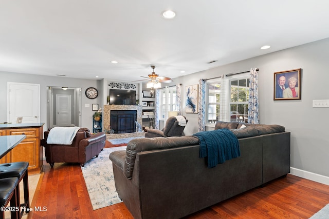 living area featuring recessed lighting, visible vents, a glass covered fireplace, wood finished floors, and baseboards