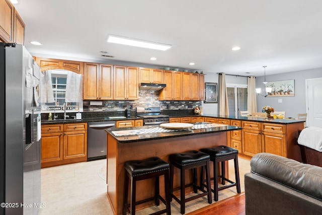 kitchen featuring a peninsula, a sink, stainless steel appliances, under cabinet range hood, and backsplash