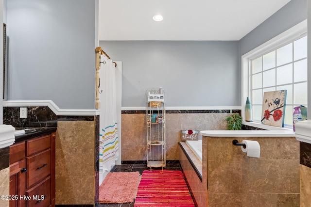 full bathroom with a relaxing tiled tub, a wainscoted wall, tile walls, recessed lighting, and tile patterned flooring