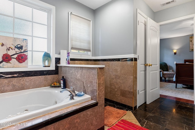 ensuite bathroom with ensuite bathroom, a tub with jets, visible vents, and tile walls