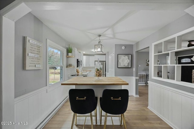 kitchen featuring a breakfast bar area, a wainscoted wall, stainless steel appliances, wood counters, and light wood-type flooring