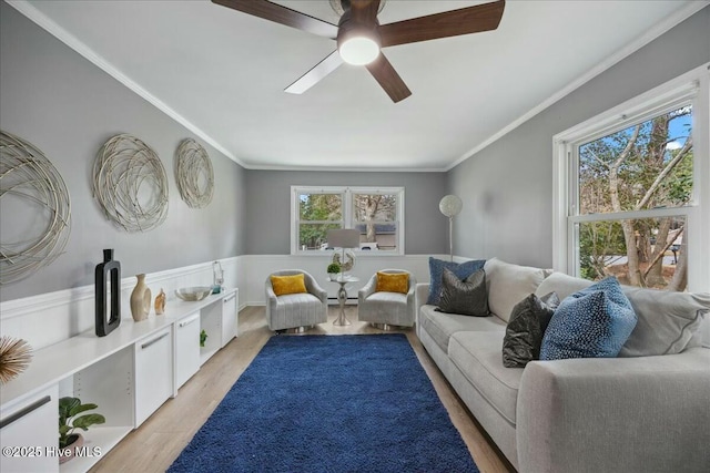 living room with ceiling fan, wainscoting, light wood-style flooring, and crown molding