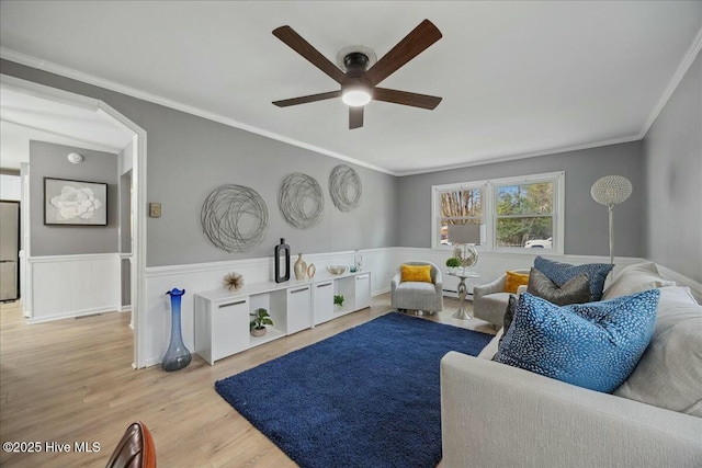 interior space featuring ceiling fan, a wainscoted wall, crown molding, and wood finished floors