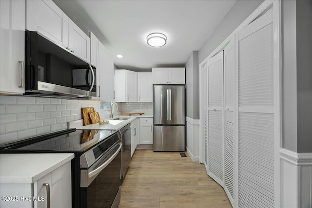 kitchen featuring light countertops, appliances with stainless steel finishes, light wood-style floors, white cabinets, and a sink