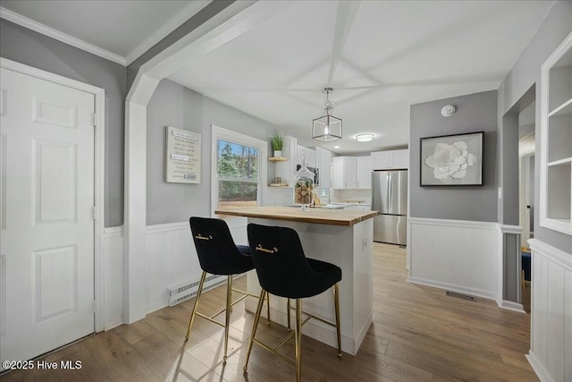 kitchen with light wood finished floors, wooden counters, freestanding refrigerator, wainscoting, and white cabinetry