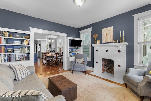 living area with a chandelier, a brick fireplace, and wood finished floors