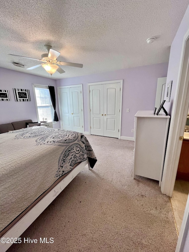 bedroom with visible vents, a ceiling fan, light colored carpet, a textured ceiling, and two closets