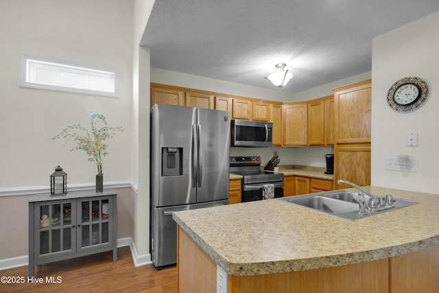 kitchen featuring light countertops, appliances with stainless steel finishes, a sink, wood finished floors, and a peninsula