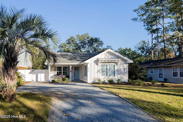 view of front of house featuring board and batten siding, driveway, a front lawn, and fence