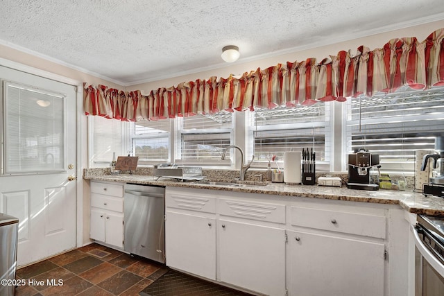 kitchen featuring stone finish floor, stainless steel appliances, a textured ceiling, white cabinetry, and a sink