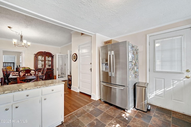 kitchen featuring an inviting chandelier, crown molding, stone tile flooring, and stainless steel fridge with ice dispenser