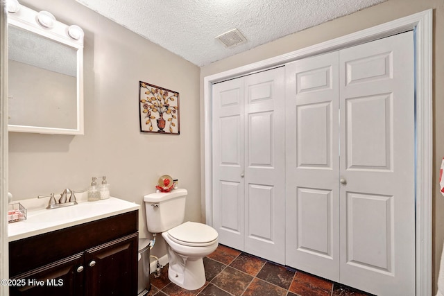 bathroom with a closet, visible vents, toilet, vanity, and a textured ceiling