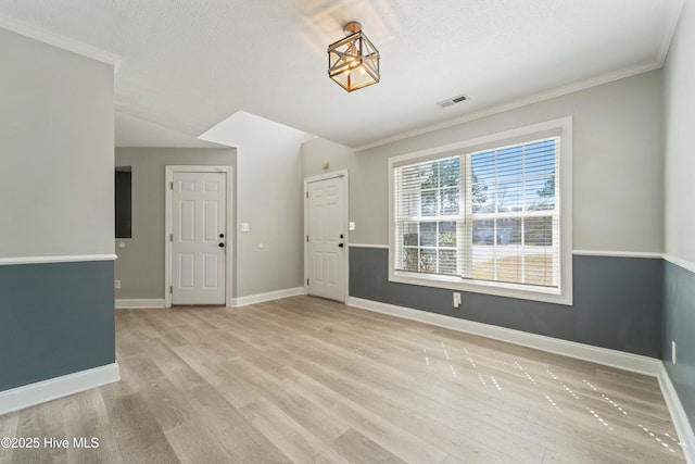 empty room featuring light wood-type flooring, baseboards, visible vents, and ornamental molding