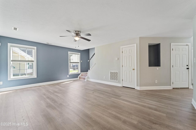 empty room featuring stairway, baseboards, visible vents, and wood finished floors